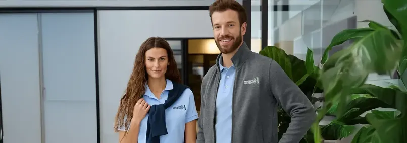 Male and female employees wearing branded light blue polo shirt and gray quarter- zip uniforms