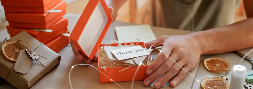 Person packaging thank you gifts in red boxes.