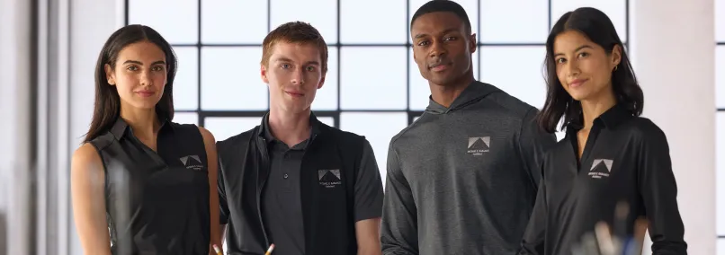 Four employees are modeling branded charcoal gray polo shirts and hoodies