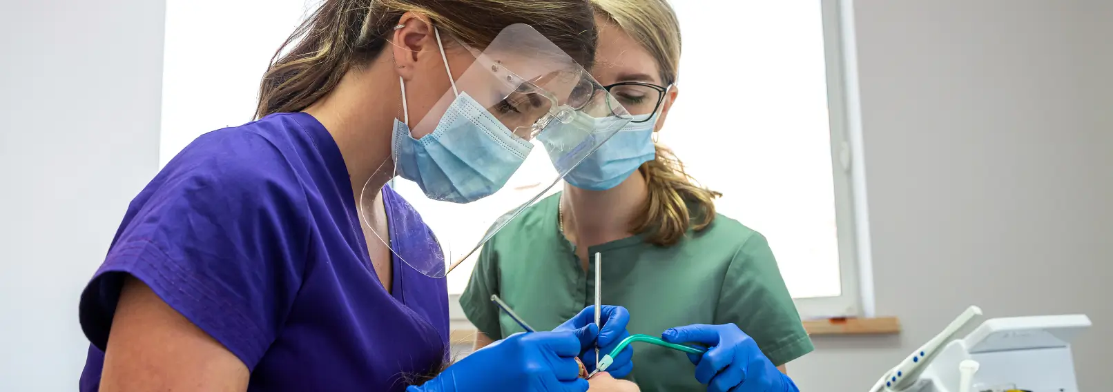 Two dental hygienists wearing scrubs working on a patient.