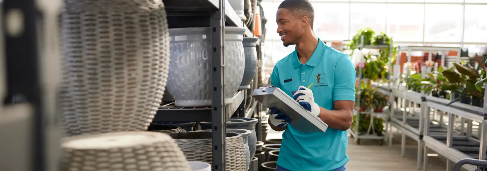 Retail employee in a teal branded polo shirt smiling in a garden center.