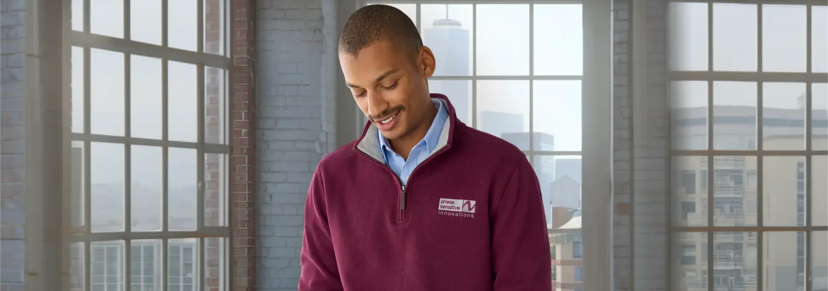 Male employee wearing a burgundy branded quarter-zip pullover in a loft-style workspace.