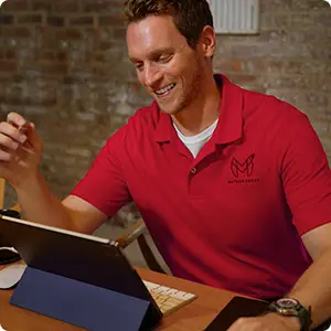 A man wearing a red polo working at a laptop.