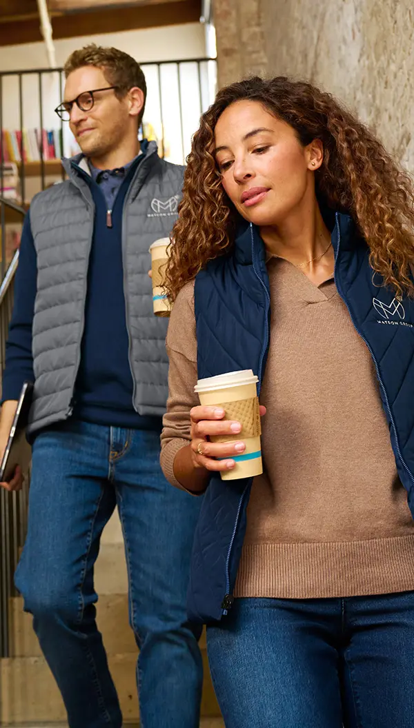 A man and a woman wearing vests with custom embroidered logos of their organization's brand.