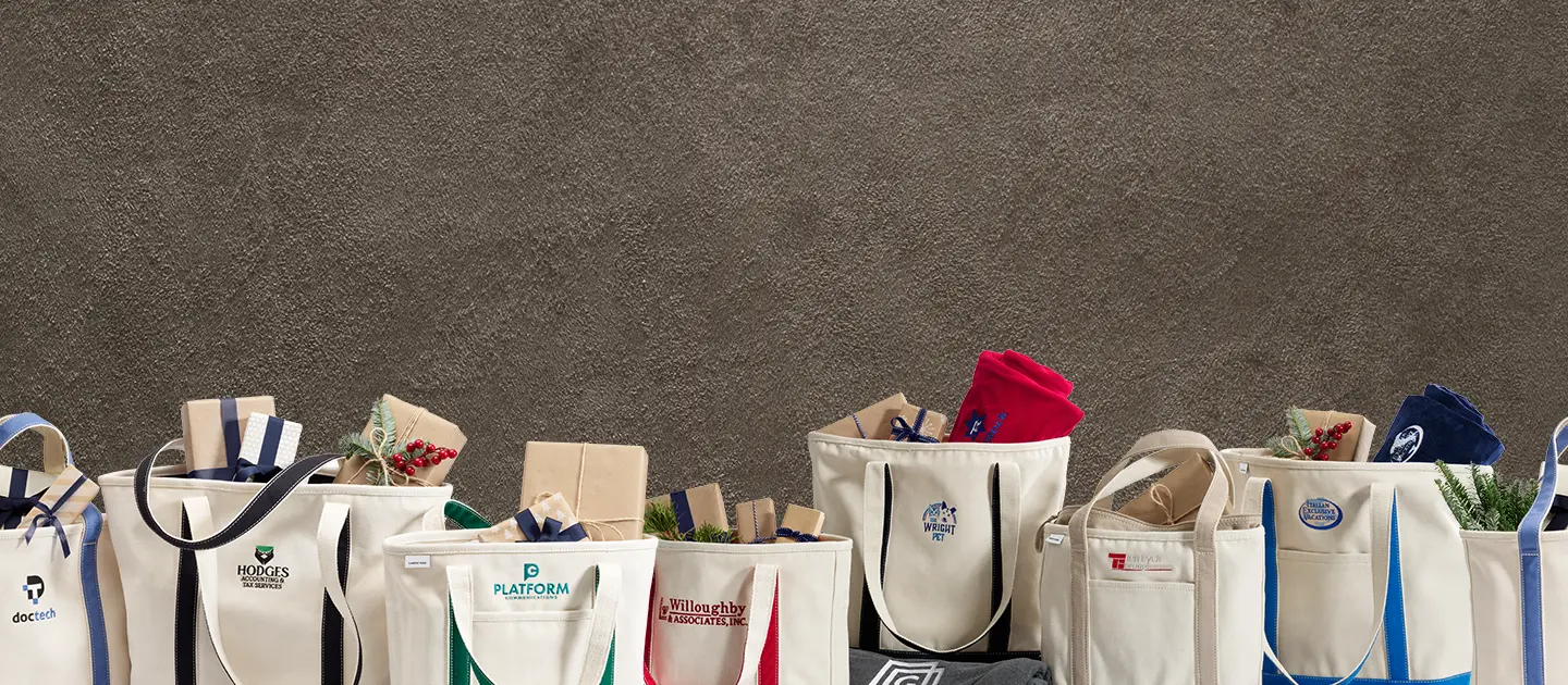 A lineup of several canvas totes packed with employee gift options.