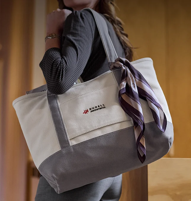 Person holding a gray-and-natural embroidered canvas tote