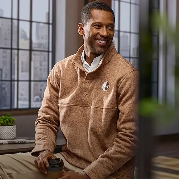 An employee wearing a brown sweater fleece drinking coffee.