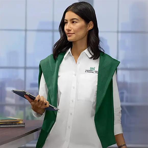 An employee holding a tablet wearing a white dress shirt with a green sweater draped over their shoulders.