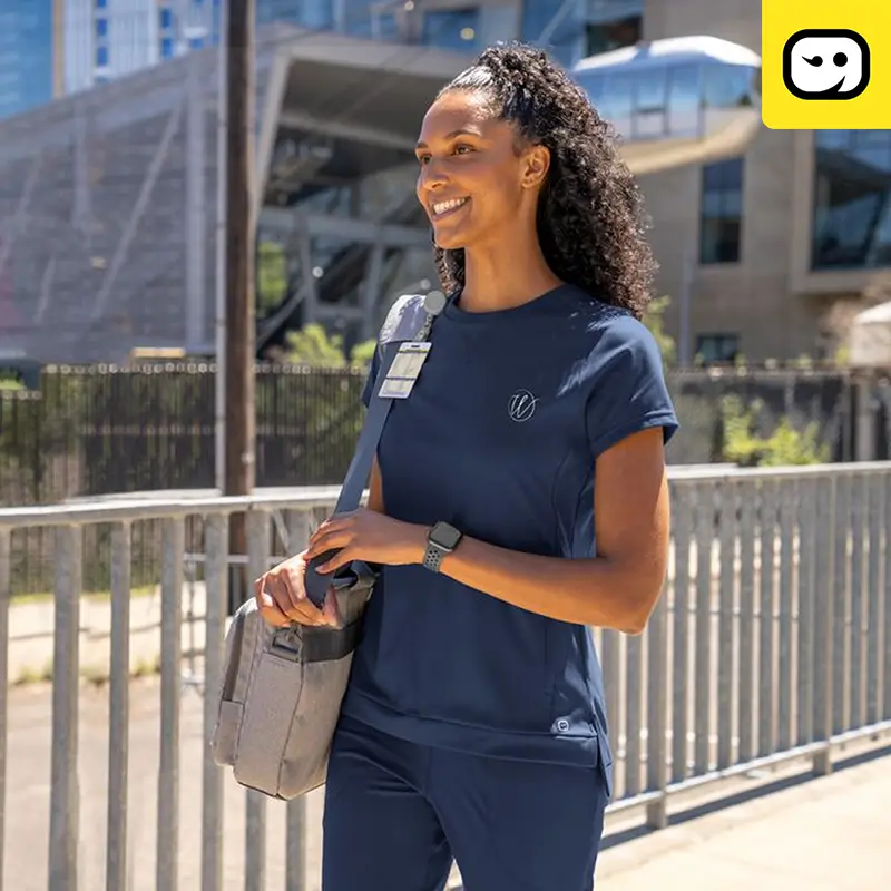 A healthcare employee wearing scrubs walking out of a facility.