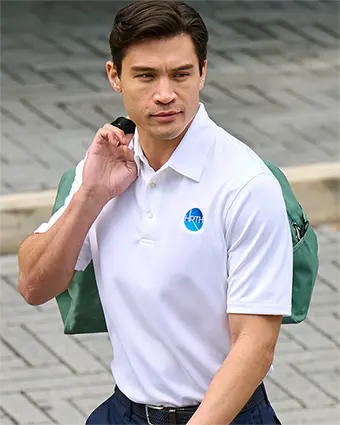 A man in a white polo holds a green bag over one shoulder