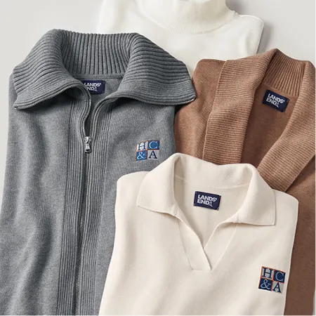 Four different sweaters in neutral colors laid on top of each other.