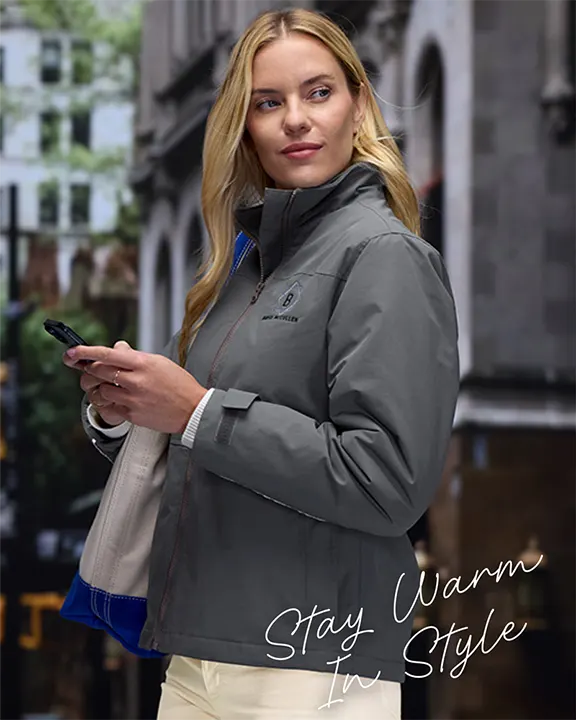 Stay Warm In Style - A woman wearing a gray jacket with a tote on her shoulder texting on her phone.