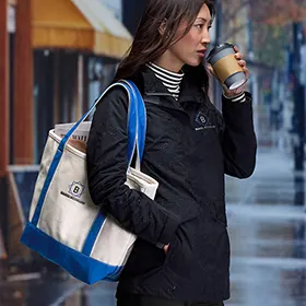 A woman wearing a black jacket with a canvas tote over her shoulder.