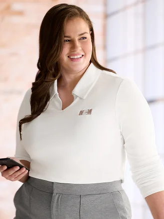 Woman wearing a white monogrammed top and grey pants.