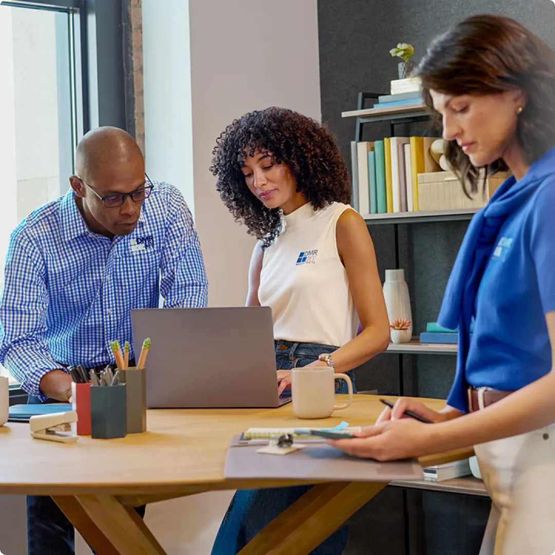 A team of employees working together, looking at a laptop and taking notes.