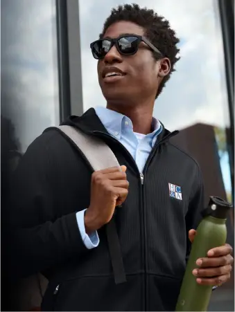A man wearing sunglasses holds a bag over his shoulder in one hand and a water bottle in the other.