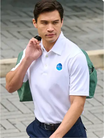 A man in a white polo holds a green bag over one shoulder